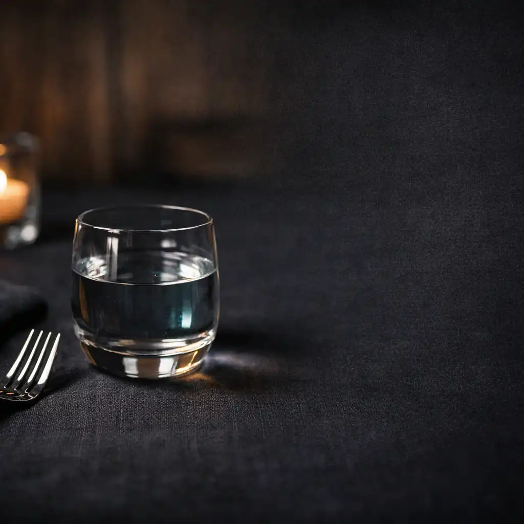 Close detail of dark linen, polished cutlery, glass and candle reflections on a restaurant table.
